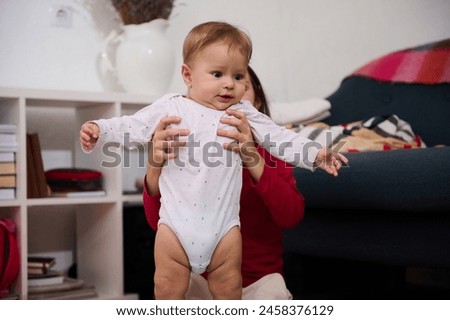Adorable baby boy in white bodysuit, in his loving caring sister's hands playing with him at home. People. Childhood. Infancy. Babyhood. Kids education nd development. The concept of happy family