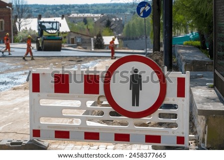 Prohibition of Pedestrian Traffic - road sign at the road construction site. Barriers on the sidewalk of a road under construction, construction machines (road roller and asphalt machine) and workers 
