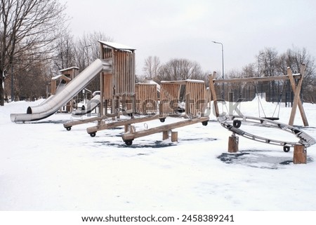 Wooden playground made of natural eco-friendly material in public city park with snow at winter time. Modern safety children outdoor equipment. Winter activities. Children rest and games on open air