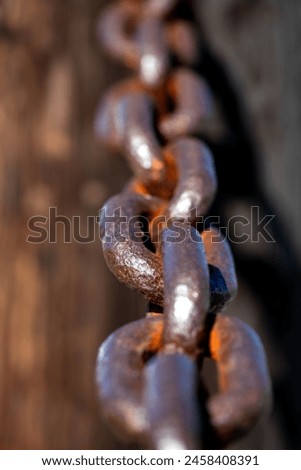Rusty and heavily weathered old chain with massive chain links. Close-up of a forged anchor chain with selective sharpness and corroded surface. Monochrome brownish colors in bright sunlight.