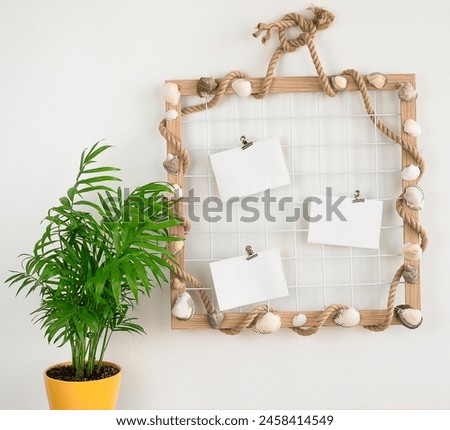 A summer mood board hangs on a white wall next to a small palm tree in a yellow pot. Summer background
