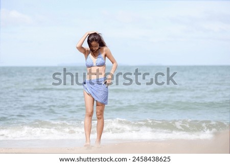 Full body back of Asian woman with bikini walking on a sunny beach with blue sea and fresh sky background. Concept of holidays and travel. Picture looking alone. Summer holiday season.