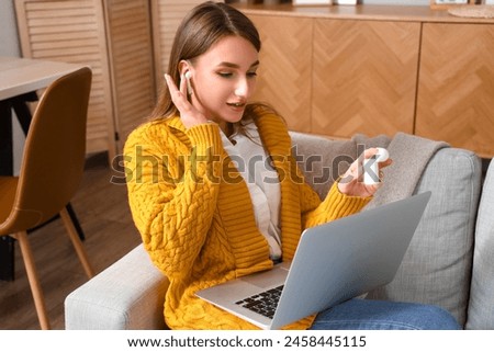 Young woman with earphones and laptop video chatting on sofa at home