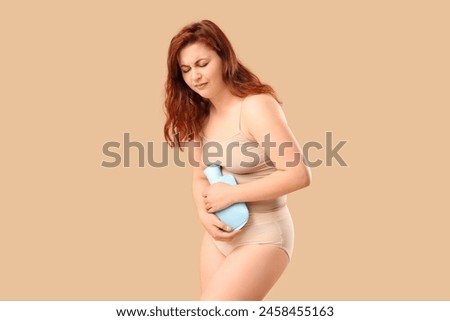 Young woman in period panties with uterus pain holding heating pad on beige background