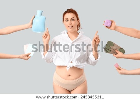 Young woman in period panties and female hands holding pads with menstrual cup and heating pad on white background Royalty-Free Stock Photo #2458455311