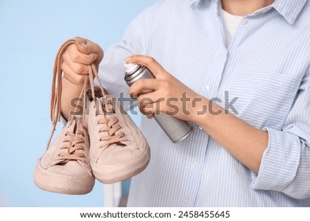 Woman applying water repellent spray over pair of gumshoes on color background, closeup Royalty-Free Stock Photo #2458455645