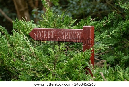 A wooden arrow shaped sign for the secret garden in ever green branches.