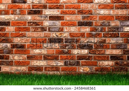 A close-up view of a red brick wall juxtaposed with a patch of vibrant green grass. The sunlight creates a warm and inviting atmosphere.Background Royalty-Free Stock Photo #2458468361