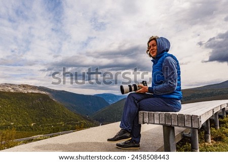 Woman with camera resting taking photo from Vedahaugane bench rest stop. National Tourist Route Aurlandsfjellet. Architecture Norway. Royalty-Free Stock Photo #2458508443