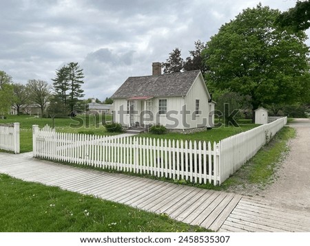 Two-room cottage where President Hoover was born in 1874. Part of the National Park Service Herbert Hoover National Historic Site in West Branch, Iowa. With fence and outhouse on a cloudy spring day. Royalty-Free Stock Photo #2458535307