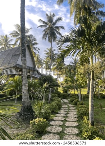 A scenic pathway leading to a cozy house surrounded by lush coconut trees. Royalty-Free Stock Photo #2458536571