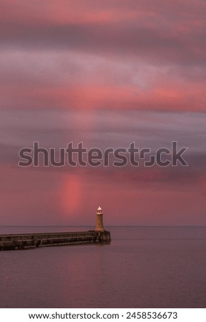A dramatic sunset lights up the cloudy sky as a vibrant rainbow appears in Tynemouth in the North East of England