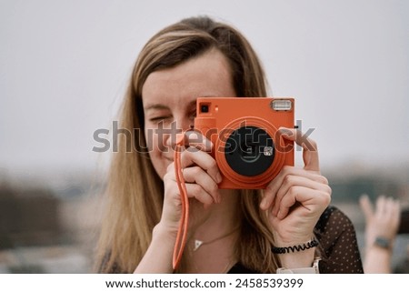 Woman taking picture using orange instant camera. Tourist captures memories during travel with vintage camera