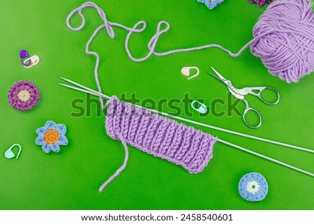 Spring knitting concept. Pattern example, traditional tools, ball of yarn, crocheted flowers. Creative handmade flat lay, bright green background, top view