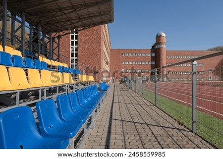 SPORTS FACILITIES - Grandstands for spectators at an athletics stadium and shool building on background Royalty-Free Stock Photo #2458559985