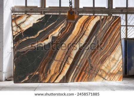 Picture of a backlit onyx slab on a hanger, shot in natural light, a cut of decorative marble in a warehouse, a large piece of marble. High resolution photo. Onyx Rainbow