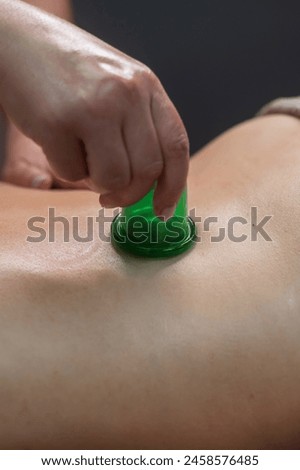 A woman undergoes an anti-cellulite massage procedure using a vacuum jar. Close-up of the lower back. Vertical photo. 