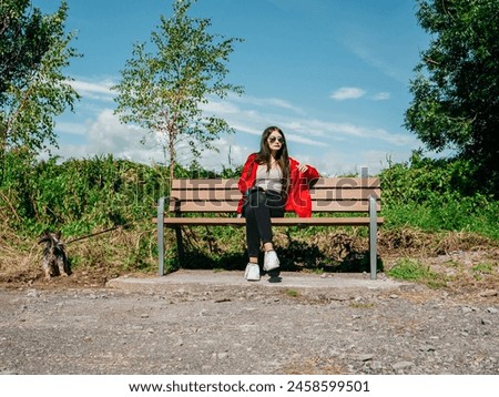 Teenager girl sitting on a bench in a park with her cute brown color Yorkshire terrier. Warm sunny day with blue sky. Looking after your pet. Enjoy fine weather. Royalty-Free Stock Photo #2458599501
