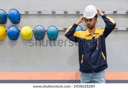 Young man working in a factory,  wearing construction hardhat on his head for safety. Concept of work safety. Building industry.