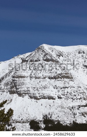 Close range of pyramid snow capped rocky Canadian mountain face with clear blue skies 