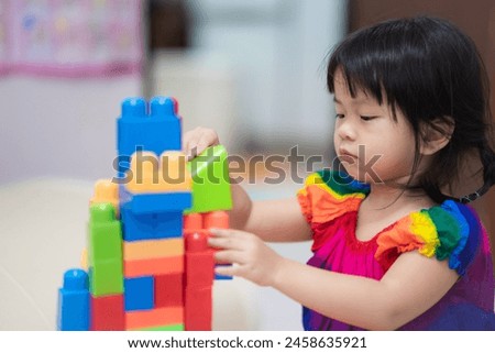 Cute Asian girl is having fun playing with colorful plastic blocks, an activity that enhances learning, enjoying a fun and educational activity, hand muscles and imagination. Child aged 3-4 years old.