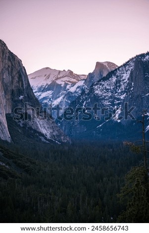 Dusky skies cast a gentle hue over the snow-laden granite peaks and forested valley of Yosemite. Royalty-Free Stock Photo #2458656743