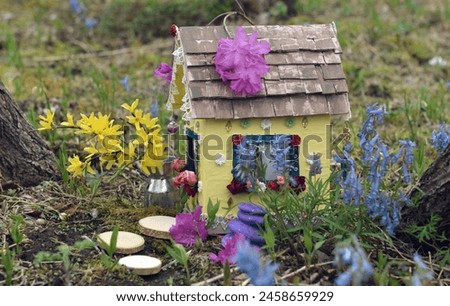 Cute fairy doll house with spring flowers outside in the garden. Lovely miniature for greeting cards, wedding or birthday concept, real estate, downsizing, home ownership. Vintage spring background