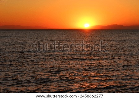 Calm dark morning sea and rising orange sun. Dawn by the sea, landscape travel photography. Distant hills over the sea and colorful sunrise.