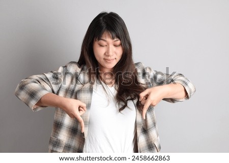 the adult Asian woman standing on the grey background, with gesture of pointing