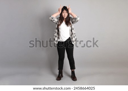 the adult Asian woman standing on the grey background, with gesture of posing