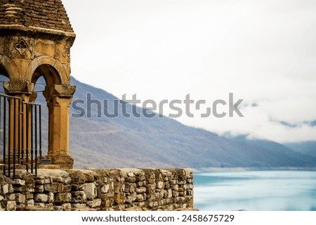 ancient stone chapel beside a tranquil mountain lake, framed against cloudy skies and distant hills historical architecture juxtaposed with natural beauty  scene history, spirituality, and nature. Royalty-Free Stock Photo #2458675729