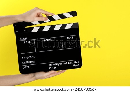 Woman holding movie clapper on yellow background, closeup. Space for text