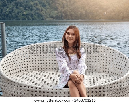 Beautiful asian woman sitting relaxing with beautiful view of lake and hills. Young woman relaxing in dress enjoying nature meditating on lake in summer