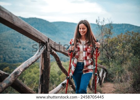 Portrait of a happy woman hiker standing on the slope of mountain ridge against mountains, blue cloudy sky on background. The woman is happy and looking at camera. Travel and active lifestyle concept.
