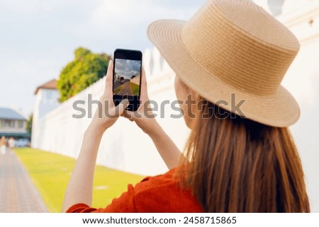 Happy young Asian woman traveler wearing orange shirt with taking photo on camera at temple or palace wall. summer tourism concept.