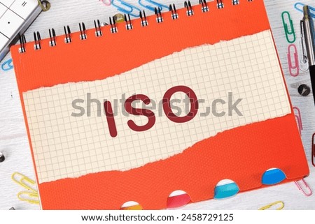 The concept of ISO quality control certification approval. Abbreviation ISO written on a piece of a sheet in a cage on the background of a notebook
