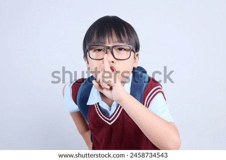 Asian schoolboy asking to be quiet with finger on lips on grey background. Keep secret and silent concept.