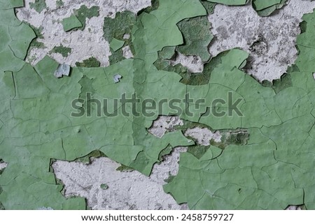 Green peeling paint on the wall. Old concrete wall with cracked flaking paint. Weathered rough painted surface with patterns of cracks and peeling. High resolution texture for background and design.