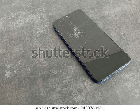 Touch phone on dark concrete background with broken screen. Old telephone on a textured concrete background.