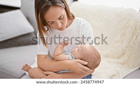 At home, joyous mother sitting on sofa, confident, lovingly trying to coax her laughing daughter into sleeping, enhancing their smile-filled relationship.