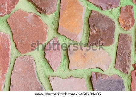 It is view of the colorful stones on green background. Its close up view of mosaic stone wall of building. It is photo of multicolored stone tile floor