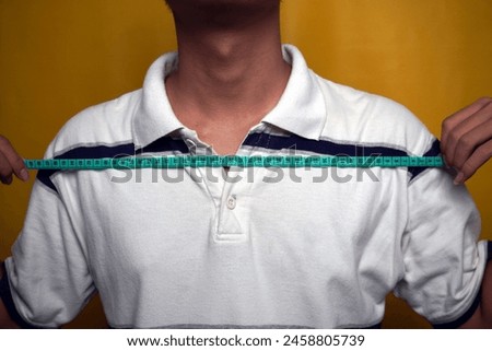 person measure the width of shoulder isolated yellow background Royalty-Free Stock Photo #2458805739