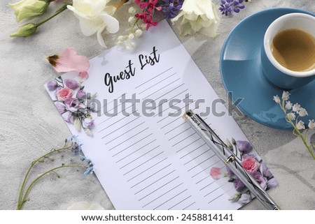 Guest list, coffee, pen and beautiful flowers on light textured table. Space for text