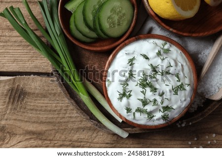 Delicious yogurt, green onion, cucumbers and dill on wooden table, top view