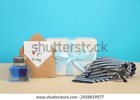 Happy Father's Day. Card with phrase I Love You, Daddy in envelope, tie, glasses, perfume and gift box on beige table