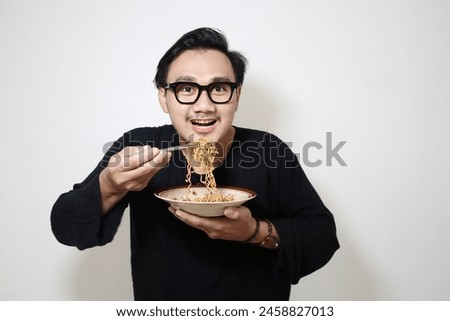 A portrait of a happy Asian man wearing a black shirt while eating noodles. Isolated with a white background.