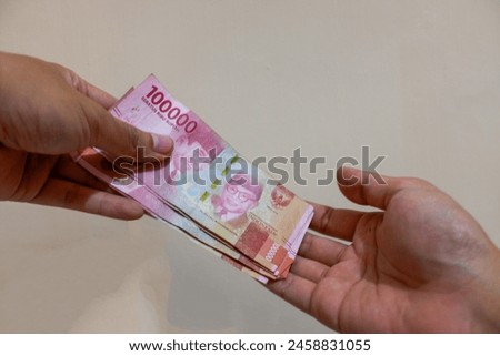 Closeup hands giving money (Rupiah) isolated on cream background, giving, stock photo. 