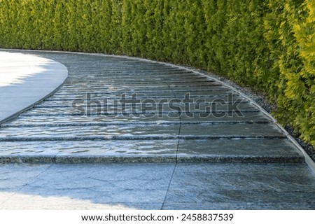 City park Krasnodar. Artificial swift river with granite banks runs around evergreen hedge with rest area. Public landscape 'Galitsky park' for relaxation and walking in sunny spring 2024 Royalty-Free Stock Photo #2458837539