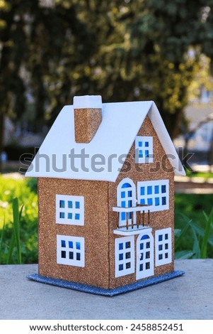 On a semi-blurred background of a park area, a brown house with blue light in the windows and a white roof
