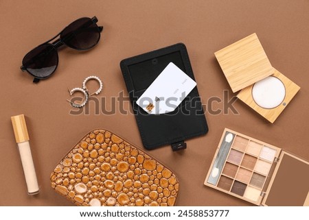 Composition with sunglasses, black holder, credit card, female bag and decorative cosmetics on brown background, closeup